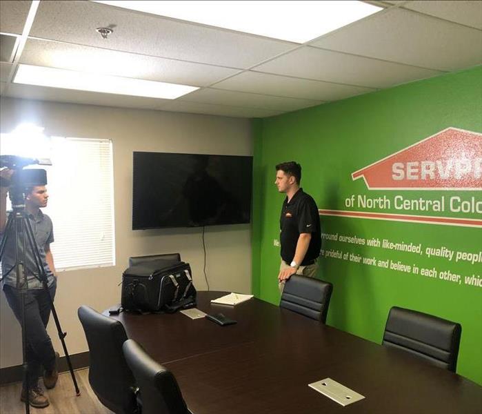 A man in front of a green SERVPRO branded wall being interviewed by a news station.