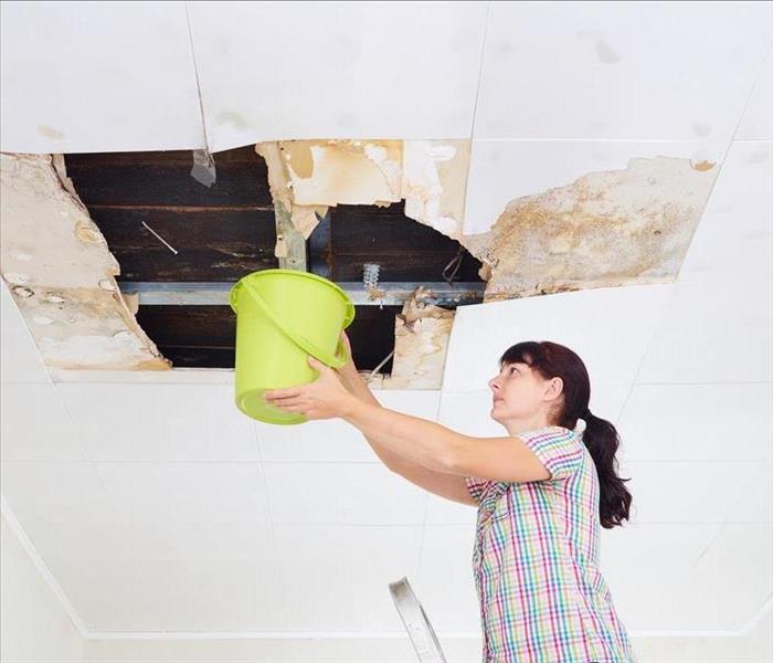 Image of a person with a bucket under a leaking water damaged ceiling 