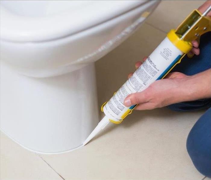 Image of a person applying caulk to a new toilet to avoid leaks